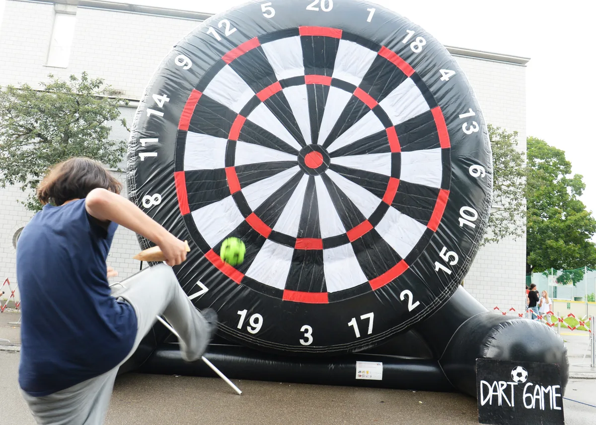 Eine Junge kickt einen Fussball auf eine riesige Dartscheibe. 